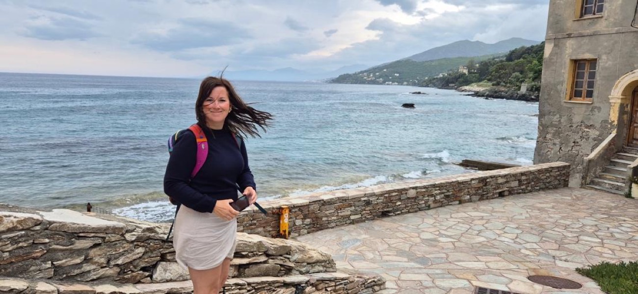 Sarah smiling on a coastal path, sea and hills behind her